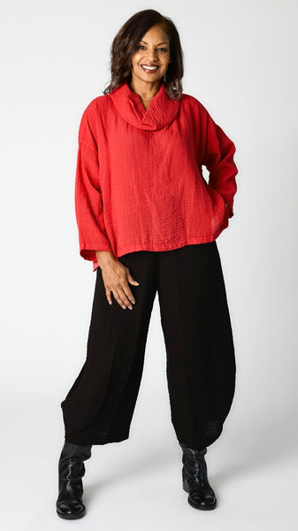 Model wearing relaxed fit rayon cowl neck top in "cinnabar" with cropped rayon tucked hem  pant in black, and black leather boots.