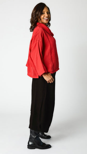 Model wearing relaxed fit rayon cowl neck top in "cinnabar" with cropped rayon tucked hem  pant in black, and black leather boots.