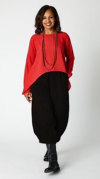 Model wearing cinnabar long sleeve cropped top with A-line silhouette, black tucked hem pant, and black leather boots.