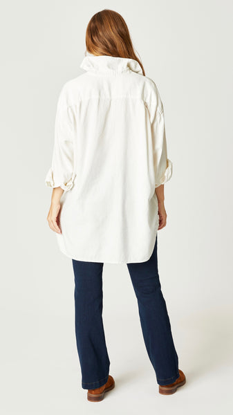 Model wearing cream off shoulder boyfriend button up top with hi-lo hemline, indigo bootcut jeans, and brown suede boots.