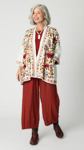 Model wearing white embroidered silk jacket over cognac cropped one size top in travel weight rayon with cognac cropped pants with ankle darts and brown leather boots.
