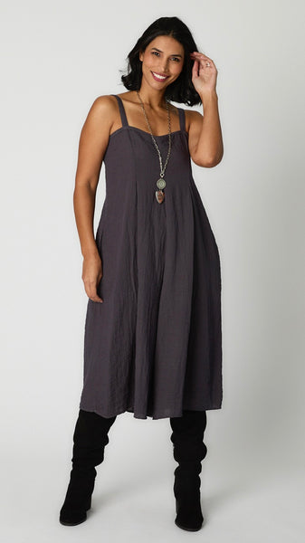 Model wearing iron rayon jumpsuit with button shoulder straps, pleat details, and wide cropped leg with black suede boots.