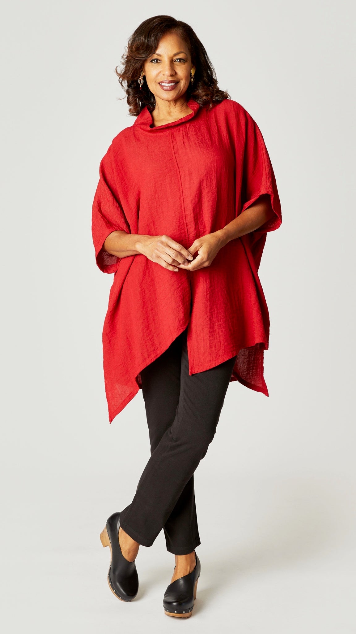 Model wearing red loose cowl neck tunic with asymmetrical hem and 3/4 sleeves, and black straight leg jeans.