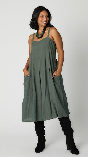 Model wearing myrtle rayon jumpsuit with button shoulder straps, pleat details, and wide cropped leg with black suede boots.