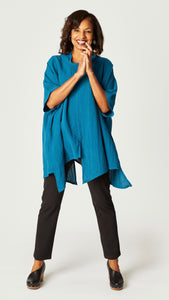 Model wearing teal loose cowl neck tunic with asymmetrical hem and 3/4 sleeves, and black straight leg jeans. 