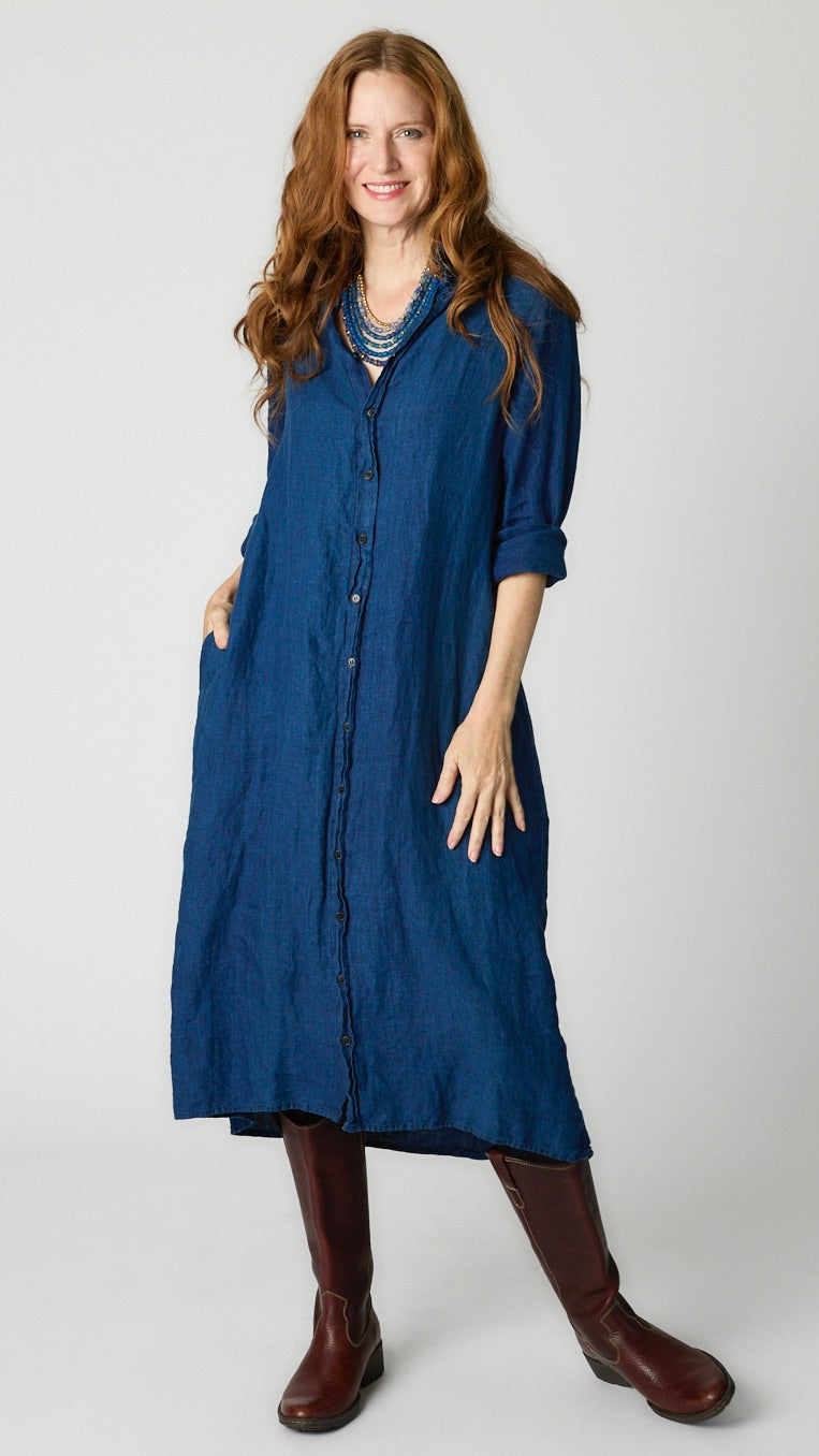 Model wearing indigo twill shirtdress with pointed collar and full length button-up panel, and brown leather boots.