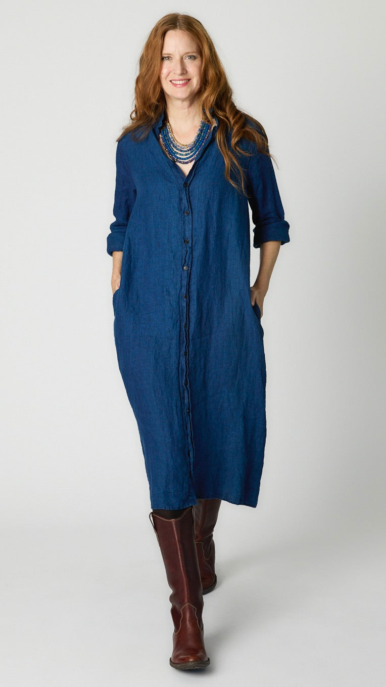 Model wearing indigo twill shirtdress with pointed collar and full length button-up panel, and brown leather boots.
