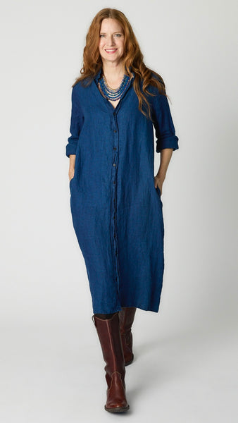 Model wearing indigo twill shirtdress with pointed collar and full length button-up panel, and brown leather boots.