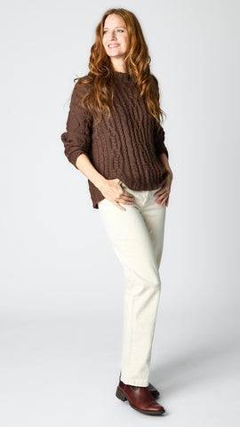 Model wearing chocolate cotton cable-knit sweater, ecru straight leg jeans, and brown leather boots. 