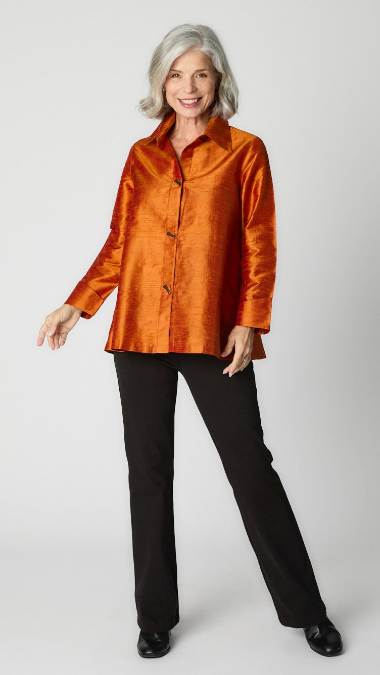 Model wearing rust raw silk button-up blouse with black horn buttons and 3/4 sleeves, black wideleg trousers, and black leather heeled boot.  