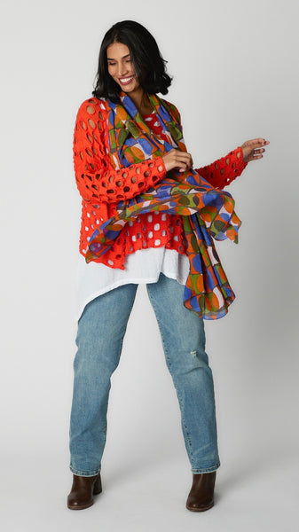 Model wearing charcoal cotton handknit sweater overlay, white rayon tunic tank, straight leg light wash jeans with brown leather stack heels, and orange and blue geometric scarf.