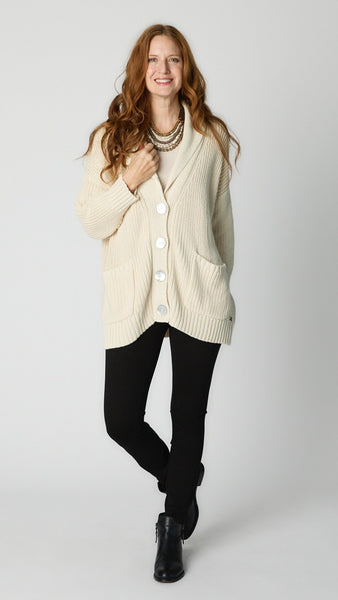 Model wearing cream cotton handknit oversized cardigan sweater over natural bias top, black denim leggings, and black leather ankle boots.