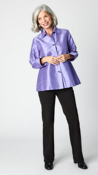 Model wearing periwinkle raw silk button-up blouse with black horn buttons and 3/4 sleeves, black straight-leg trousers, and black leather heeled boot.  