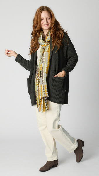 Model wearing charcoal cotton handknit oversized cardigan (without buttons) over natural bias top, ecru straight leg denim pant, and taupe suede boot. 