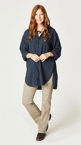 Model wearing ink relax fit button-up shirt with long sleeves, front pocket, and hi-lo hemline, with geode necklace, taupe bootcut jeans, and black boots. 