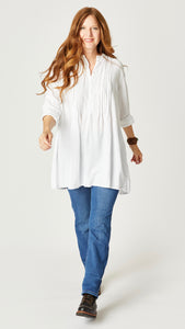 Model wearing white double cotton tunic with front button, long sleeves, pleating at yoke, and midwash straight leg jeans.