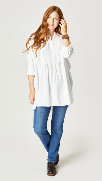 Model wearing white double cotton tunic with front button, long sleeves, pleating at yoke, and midwash straight leg jeans.