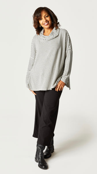 Model wearing white and gray striped cowl neck top with dolman sleeves and A-line silhouette. Black cropped pant, and black leather boots.