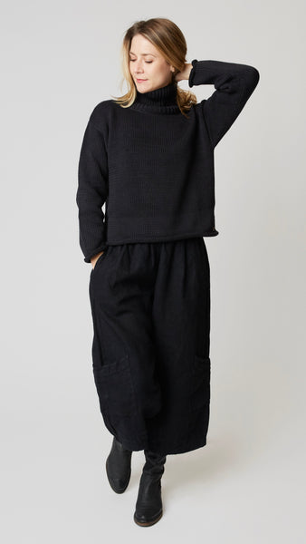 Model wearing black handknit cotton turtleneck sweater (slightly cropped), with black heavyweight linen cropped pant with side pockets above ankle darts, and black leather boots.