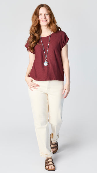 Model wearing cognac cotton-linen jersey top with cropped sleeves, boatneck, and boxy silhouette with ecru straight leg jeans and brown sandals.