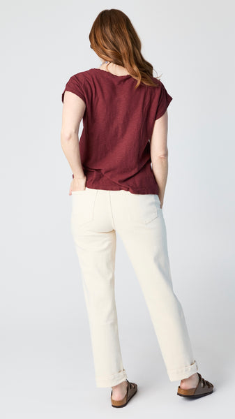 Model wearing cognac cotton-linen jersey top with cropped sleeves, boatneck, and boxy silhouette with ecru straight leg jeans and brown sandals.