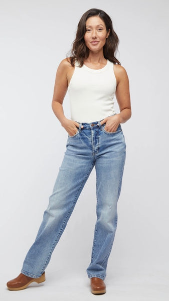 Model wearing white tank top, straight-leg, high-waisted mid-wash jean, and light brown clogs. 