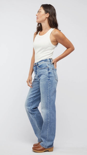 Model wearing white tank top, straight-leg, high-waisted mid-wash jean, and light brown clogs. 