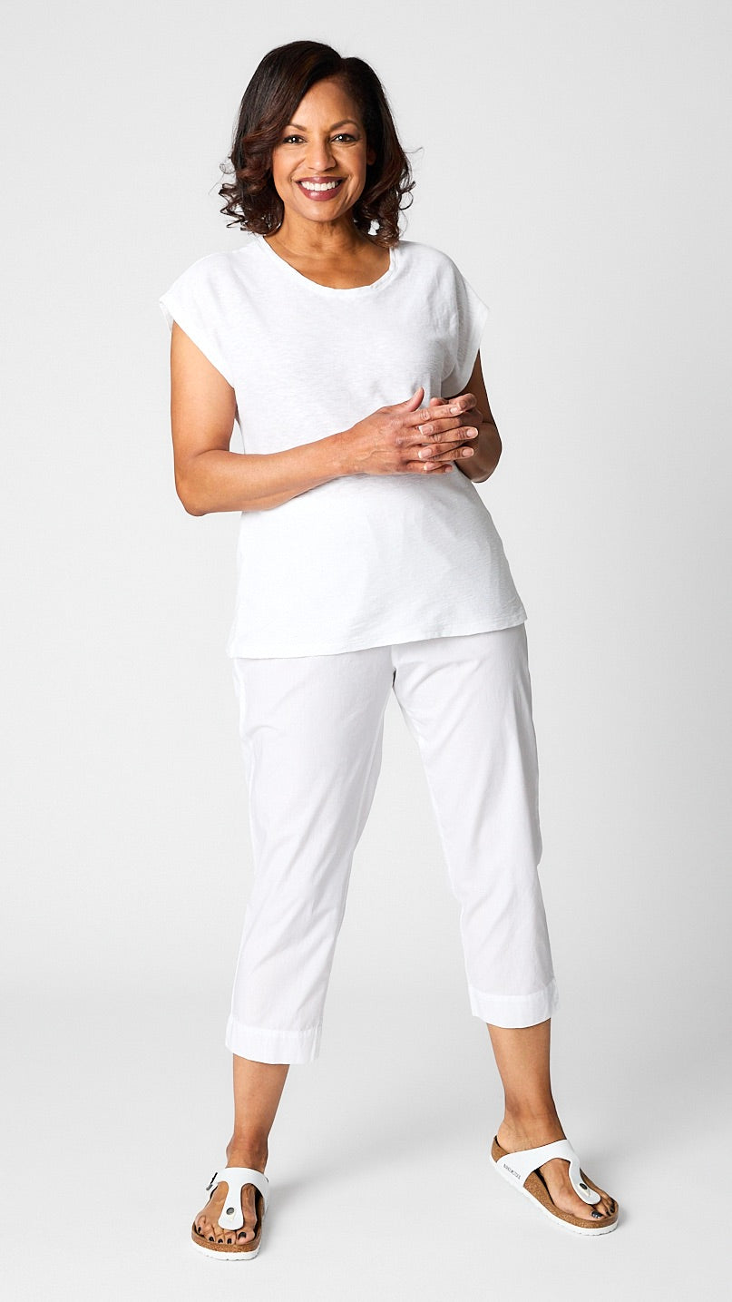 Model posing in white cropped sleeve box top, white tapered cropped pants in organic poplin, and white sandals. 