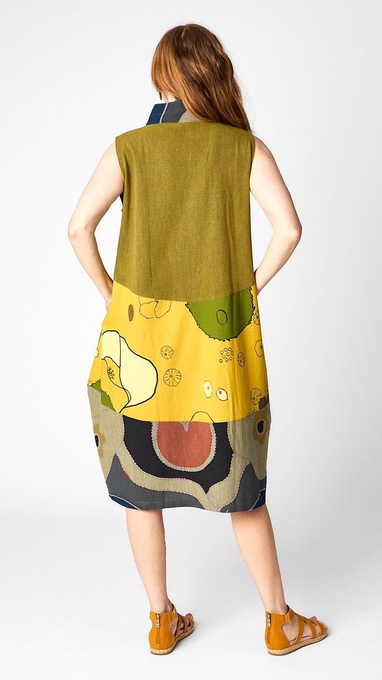 Rear view of model wearing kasur dress/vest shows three tiers of assorted mustard yellow fabrics. 