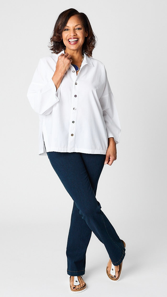 Model wearing "chalk" white button-up top with relaxed hemline and 3/4 sleeves over indigo baby bootcut jeans and white sandals.