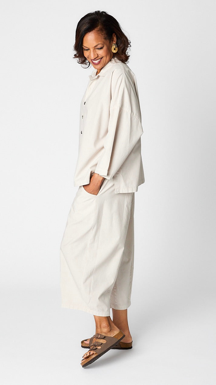 Model wearing cloud button-up top with relaxed hemline and 3/4 sleeves over cloud cropped one pocket pants and brown sandals.