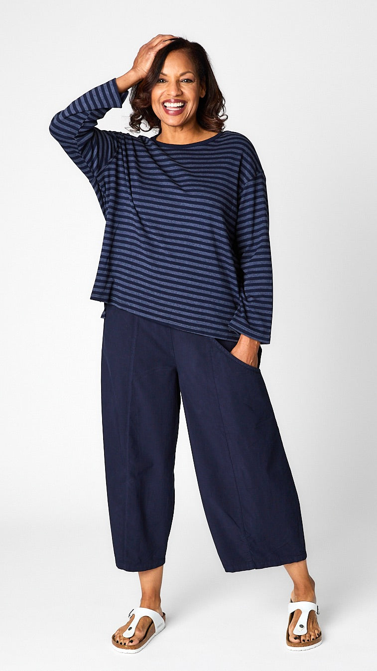 Model wearing "indigo" striped relaxed long sleeve tee, "indigo" cropped pant with one pocket, and white leather sandals.