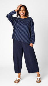 Model wearing "indigo" striped relaxed long sleeve tee, "indigo" cropped pant with one pocket, and white leather sandals.