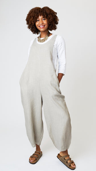 Model wearing rye linen overalls with cropped dart legs, white 3/4 sleeve top, beaded leather necklace, and brown suede sandals.