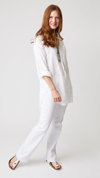 Model wearing white linen button up tunic top with front pocket, white bootcut jeans, and white sandals.