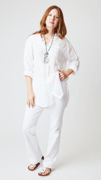 Model wearing white linen button up tunic top with front pocket, white bootcut jeans, and white sandals. 