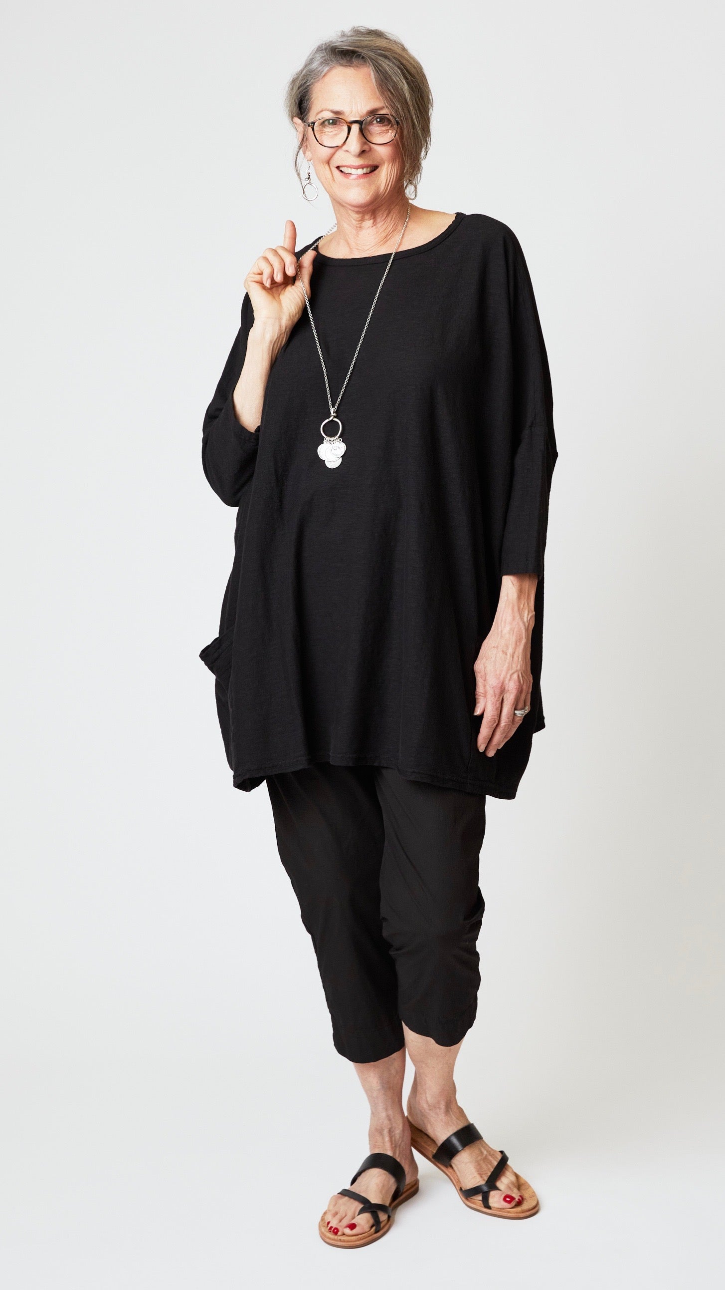 Model wearing black one size roomy two pocket tunic top, black tapered cropped pant in organic poplin, and black sandals. 