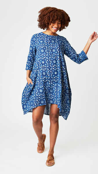 Model wearing "cairo indigo" block print tunic dress with 3/4 sleeves, high-low hemline and bubble silhouette, with brown leather sandals.