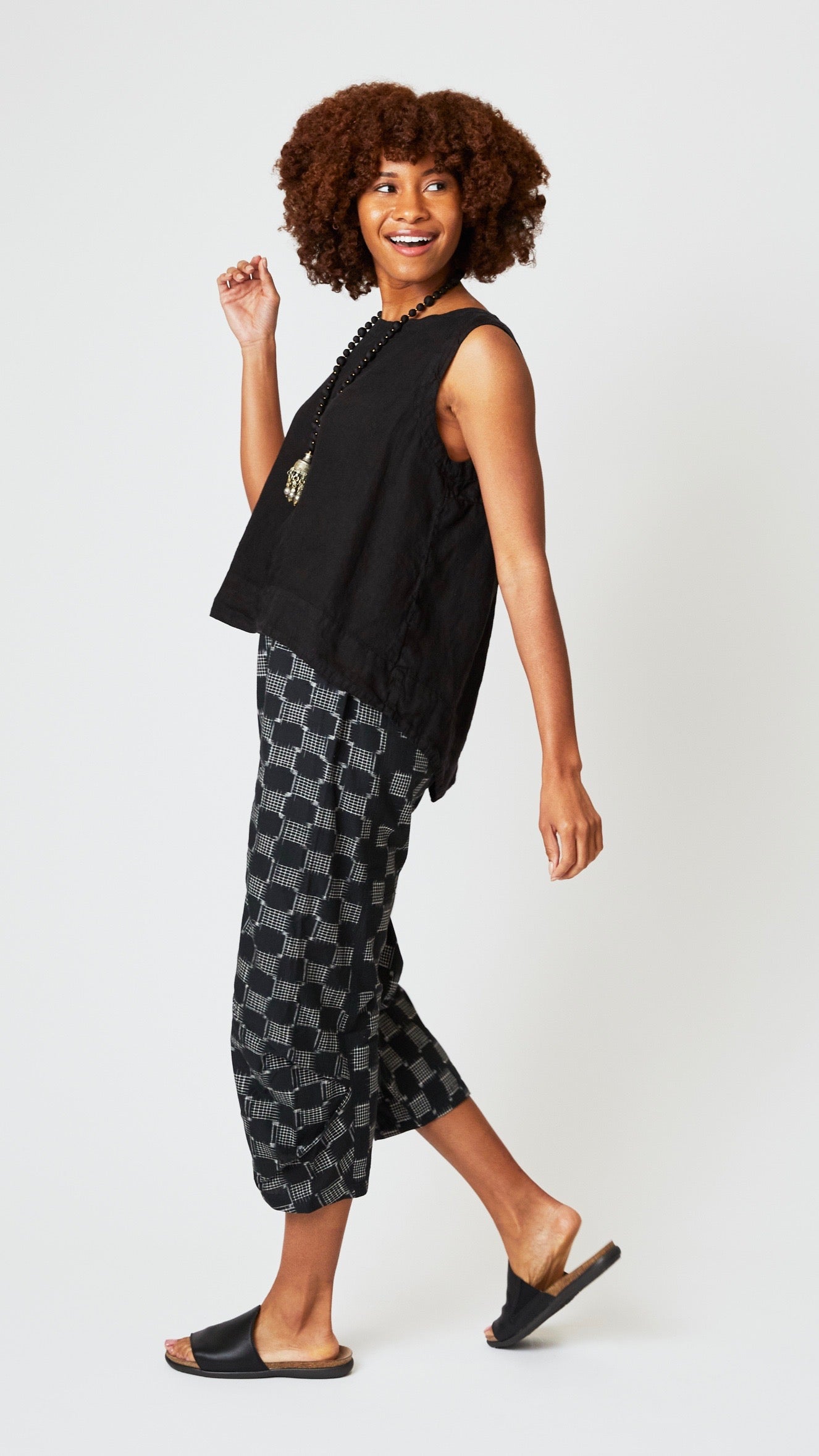 Model wearing black linen sleeveless tank with hi-lo silhouette, and black and white ikat cropped linen pants with darts.  