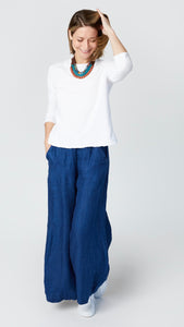 Model wearing high-waisted pants with wide-leg, flat front elastic waistband and side pockets, with white cotton/linen jersey bias cut top with 3/4 sleeves, and white sneakers. 