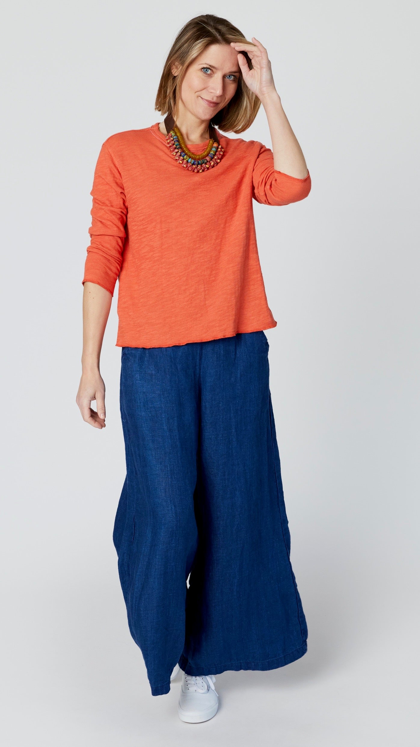 Model wearing high-waisted pants with wide-leg, flat front elastic waistband and side pockets, with orange long sleeve t-shirt, and white sneakers.