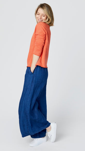 Model wearing high-waisted pants with wide-leg, flat front elastic waistband and side pockets, with orange long sleeve t-shirt, and white sneakers.