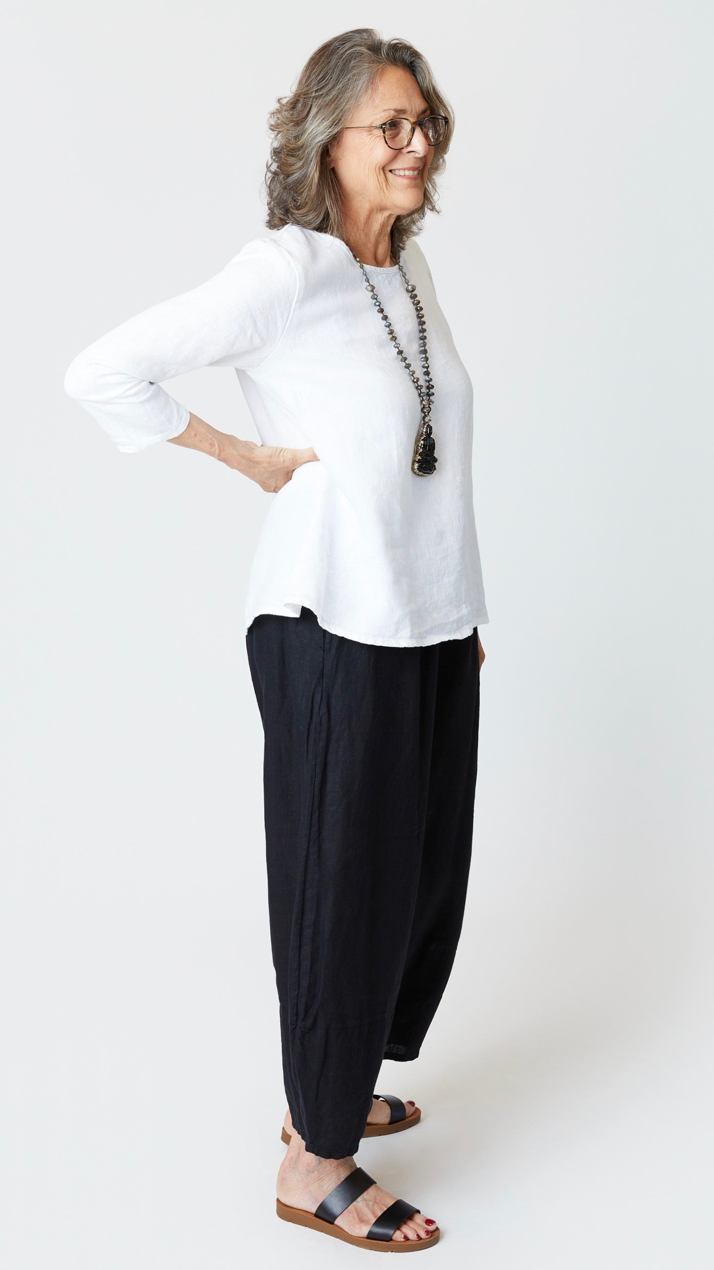 Model wearing white 3/4 sleeve A-Line linen top, black linen lantern pants, beaded necklace, and black leather sandals.