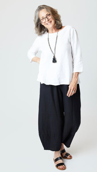 Model wearing white 3/4 sleeve A-Line linen top, black linen lantern pants, beaded necklace, and black leather sandals.