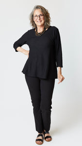 Model wearing black cotton-linen jersey top with 3/4 sleeves, hidden side pockets, and unfinished neckline, black straight leg jeans, and black sandals.