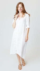 Model wearing white linen shirtdress with pointed collar and full length button-up panel, and tan leather sandals. 