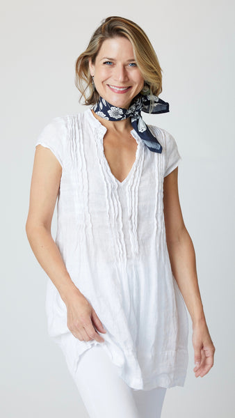 Model wearing chambray linen tunic with pin-tucked bodice, v-neck, and cap sleeves, with white bootcut jeans, and navy and white floral handkerchief.