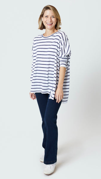 Model wearing navy and white striped cotton tee with dropped shoulder 3/4 sleeve and side slits, indigo bootcut jeans, and white sneakers.