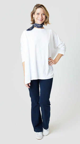 Model wearing white cotton tee with dropped shoulder 3/4 sleeve and side slits, indigo bootcut jeans, and white sneakers.