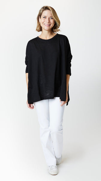 Model wearing black cotton tee with dropped shoulder 3/4 sleeve and side slits, white bootcut jeans, and white sneakers.